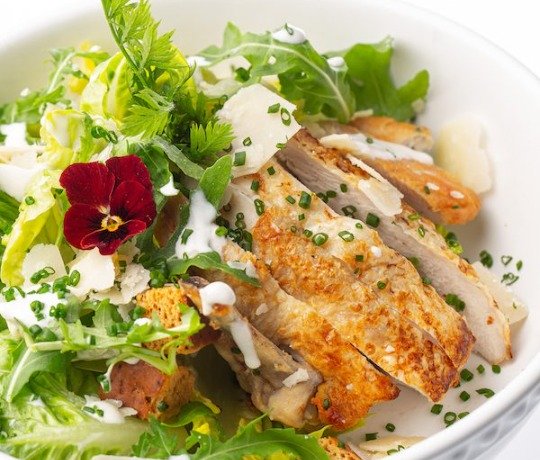 World Class private jet catering from 3Flavours Chicken caesar salad in a white bowl garnished with a red flower